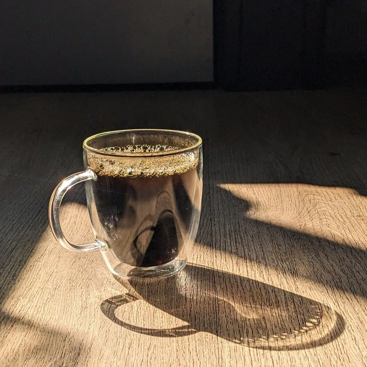 Glass cup of black coffee casting a long shadow in the morning sunlight